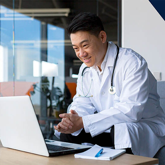 Doctor on laptop looking at course content with pen and paper